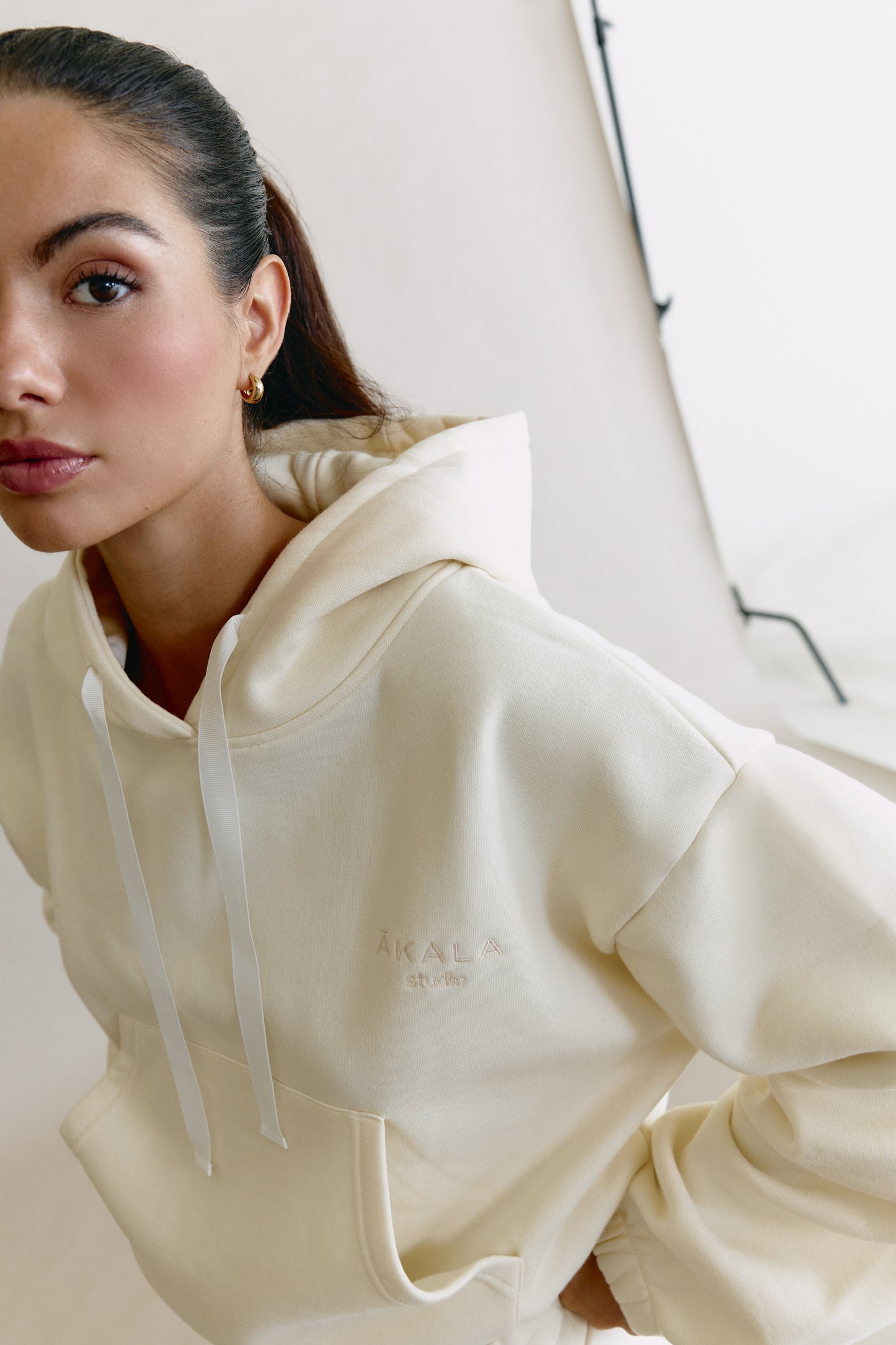 Woman wearing a cream-colored hoodie with a brand logo on a neutral background