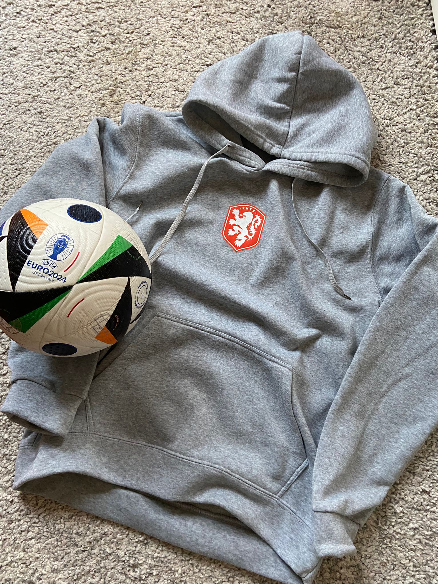 Gray hoodie with a logo next to a soccer ball on a carpeted floor