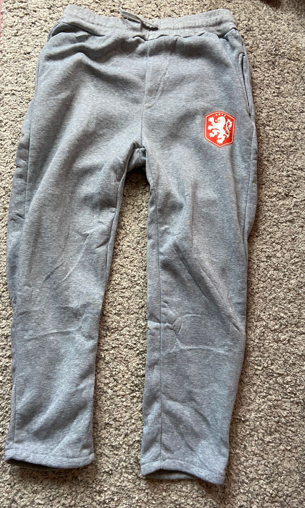 Gray sweatpants with a red and white logo on a beige carpet