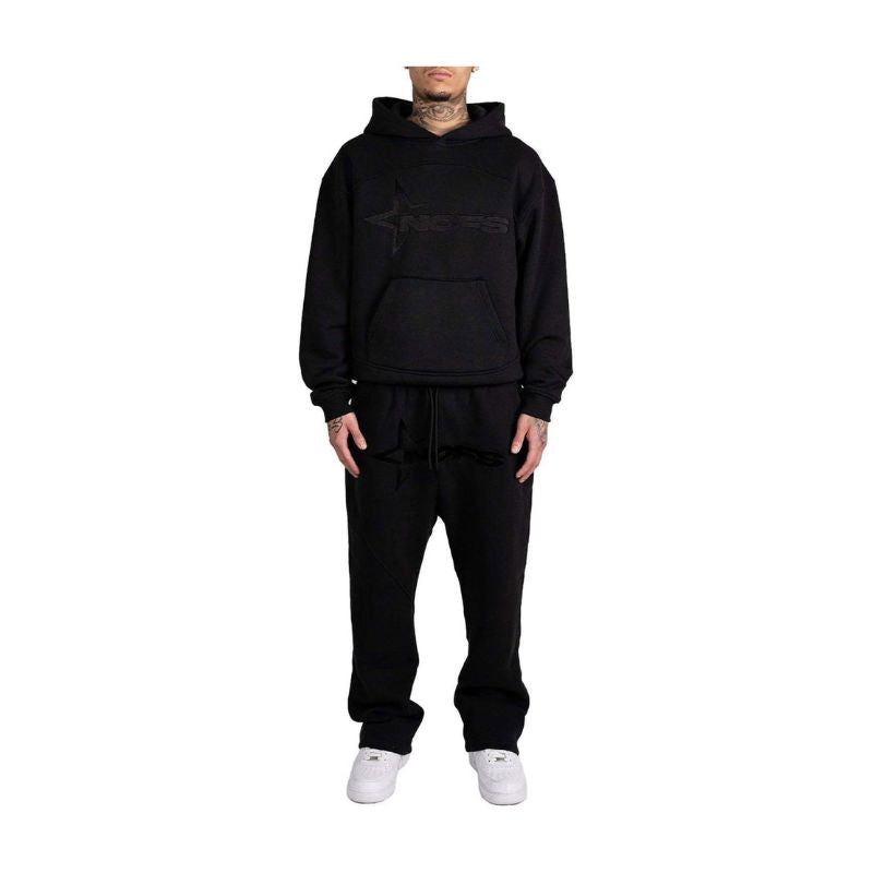 Person wearing a black hoodie and pants set with a brand logo on a white background