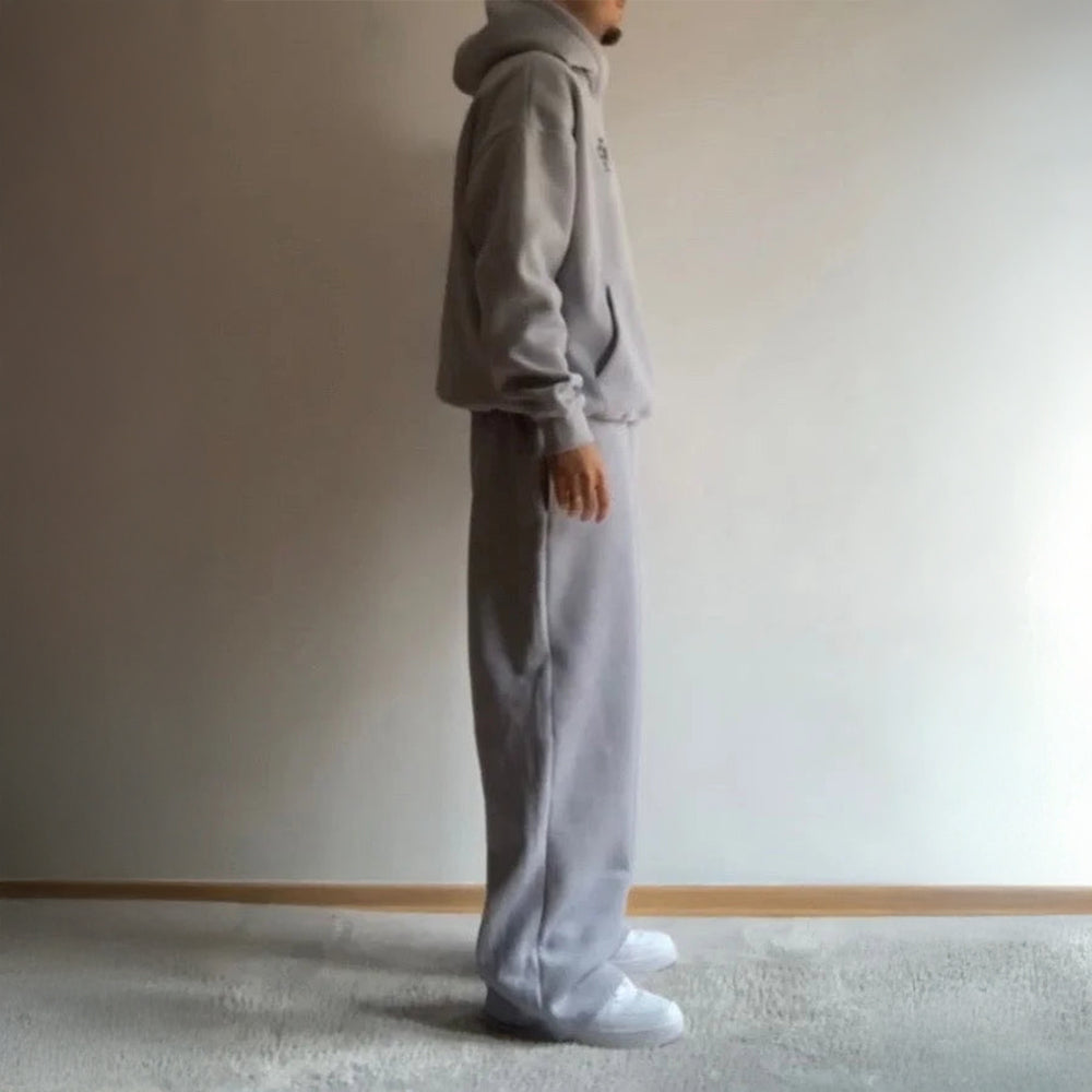 Person wearing a gray tracksuit standing against a plain wall.