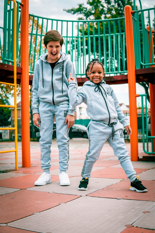 Two children in matching gray tracksuits standing on a playground.