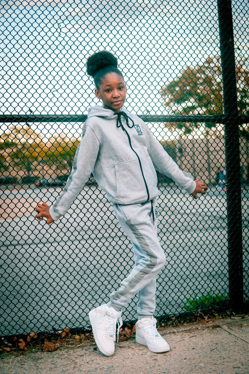 Person wearing a gray tracksuit standing in front of a chain-link fence.