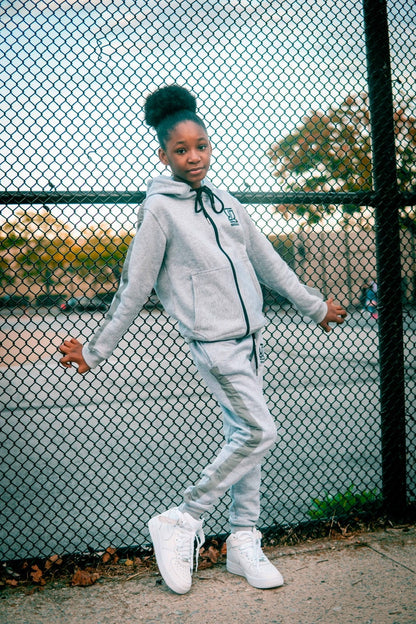 Person wearing a gray tracksuit standing in front of a chain-link fence.