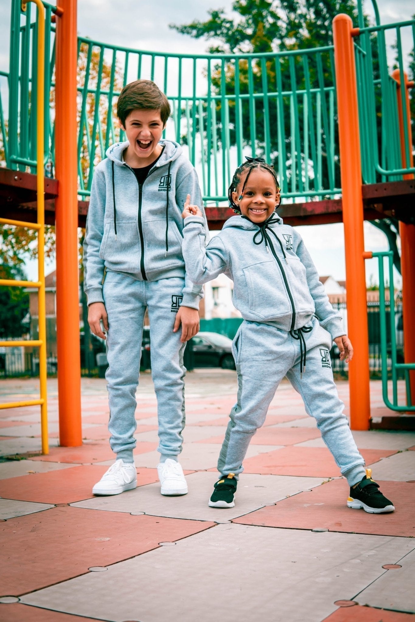 Two children in matching gray tracksuits on a playground.