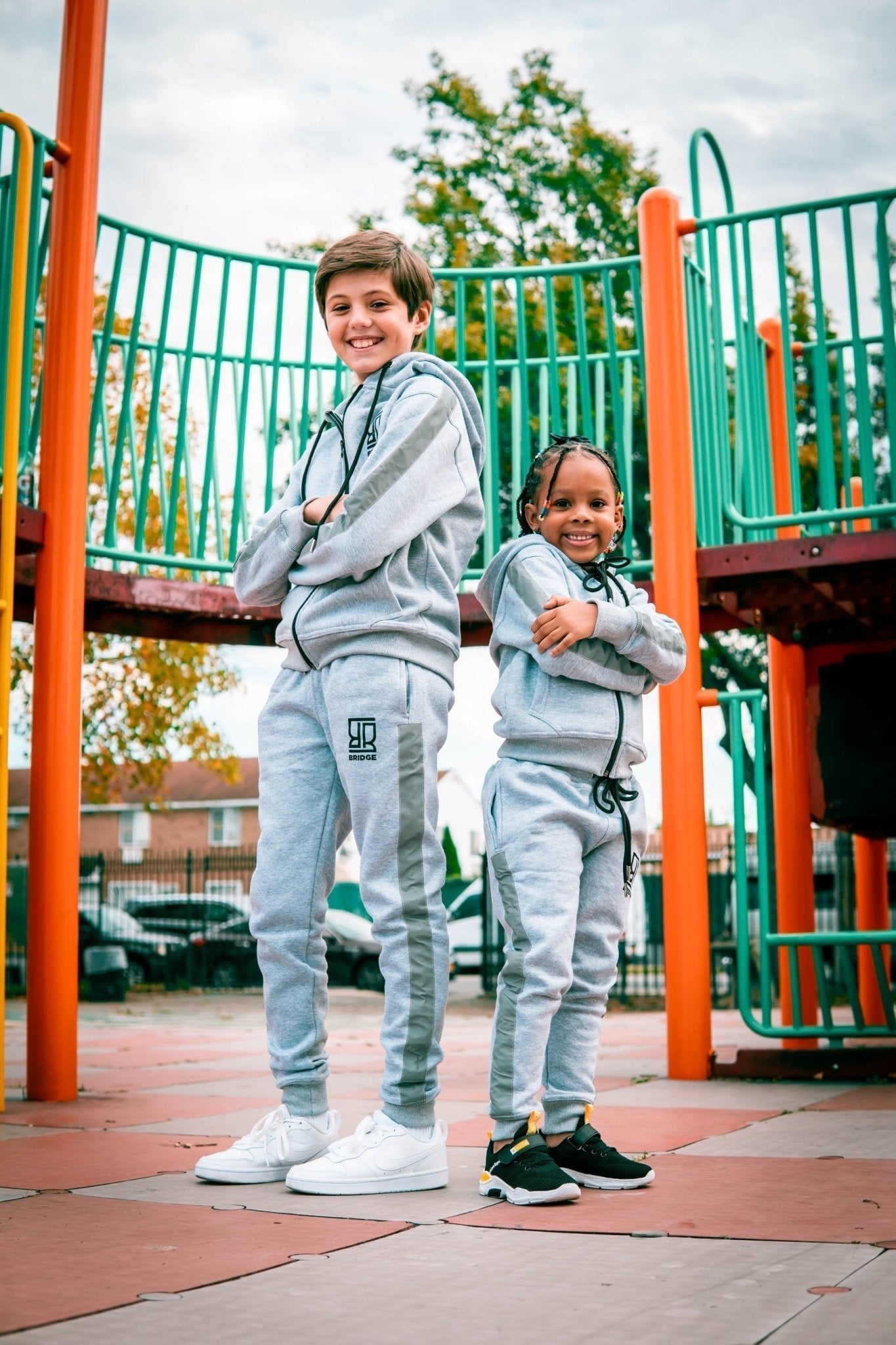Two children in matching gray tracksuits standing on a playground.