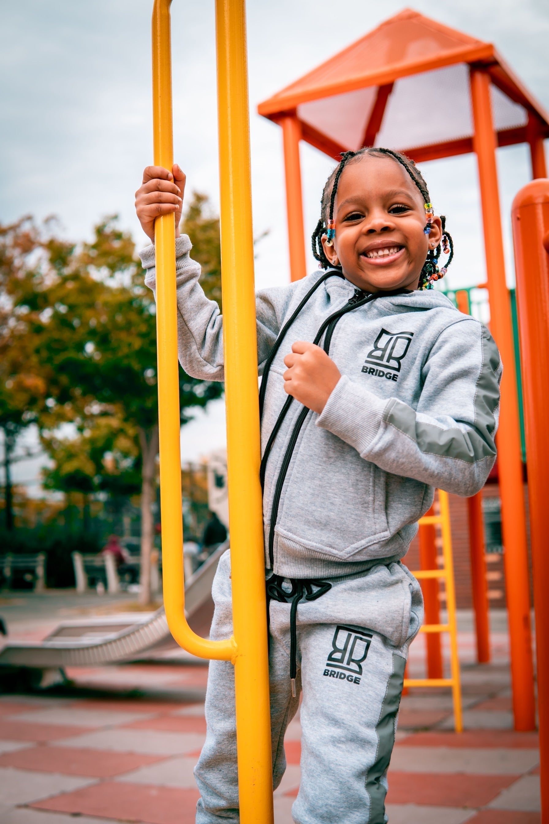 Child in a gray tracksuit on a playground with yellow bars