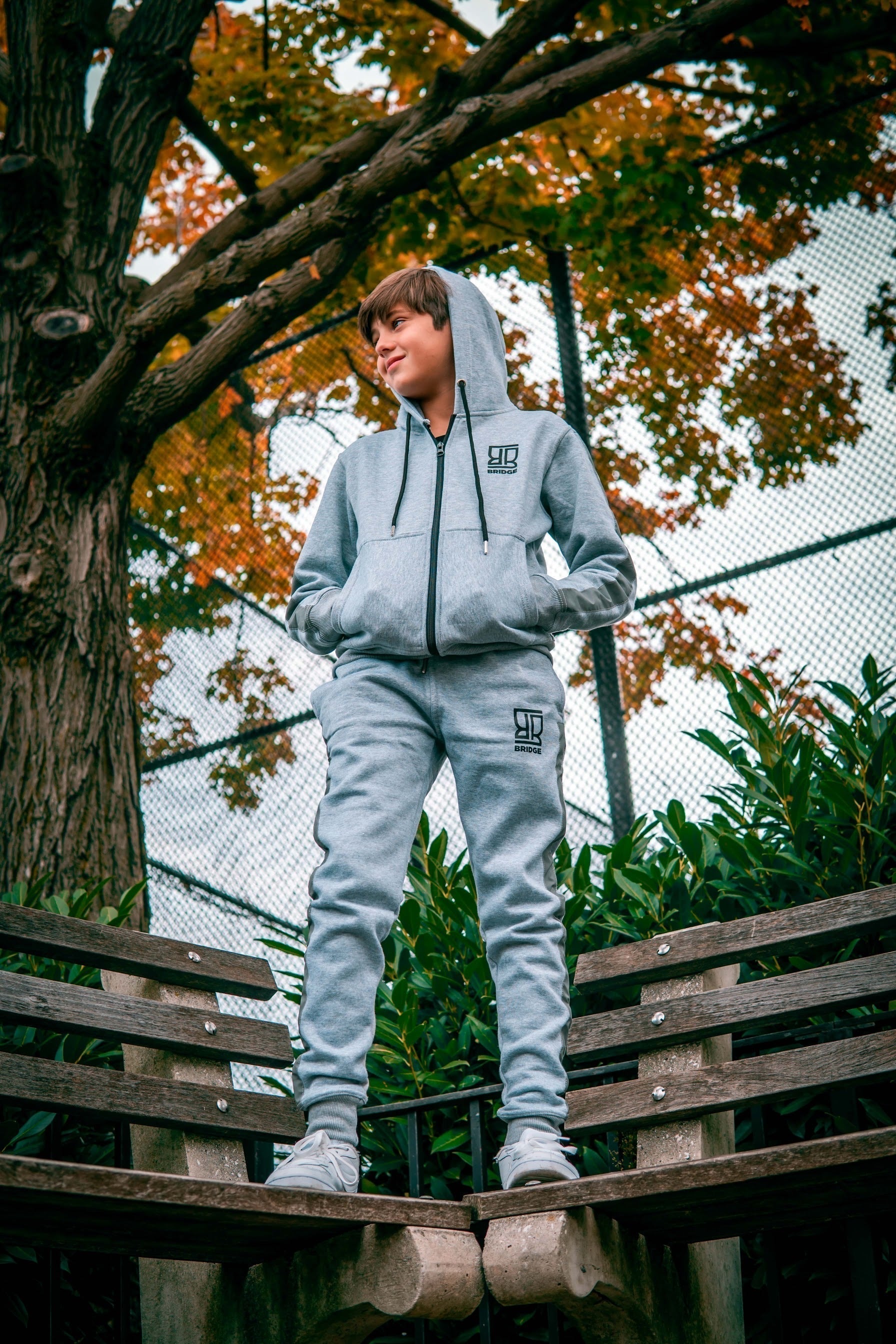 Person wearing a gray tracksuit standing on a wooden bench with trees and greenery in the background