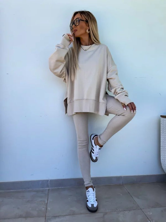 Woman in beige sweatshirt and leggings standing against a light blue wall.