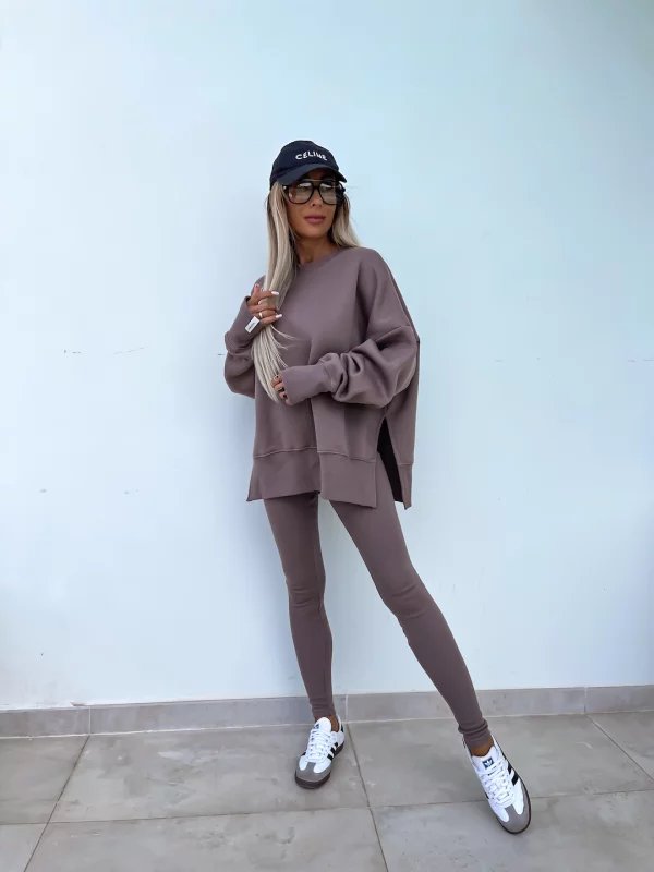 Person wearing a matching brown outfit with a cap against a light blue wall.