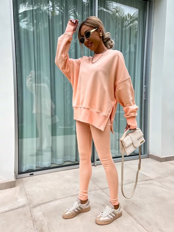 Woman in peach sweatshirt and leggings standing in front of a glass door.