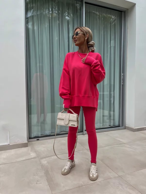 Person wearing a bright pink outfit with a white handbag, standing in front of a glass door.