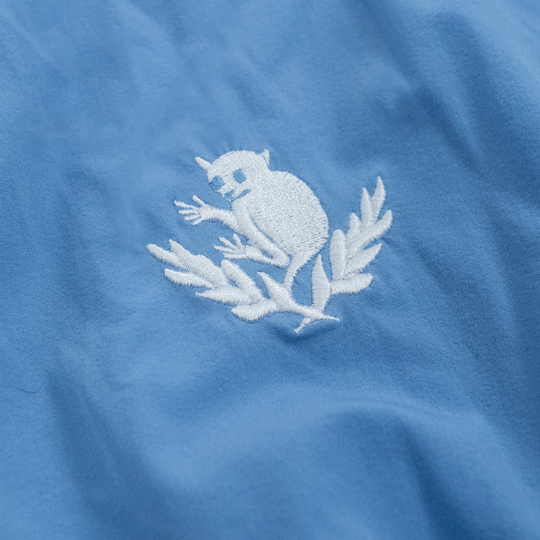 Close-up of a blue fabric with a white embroidered design of a cat and leaves.