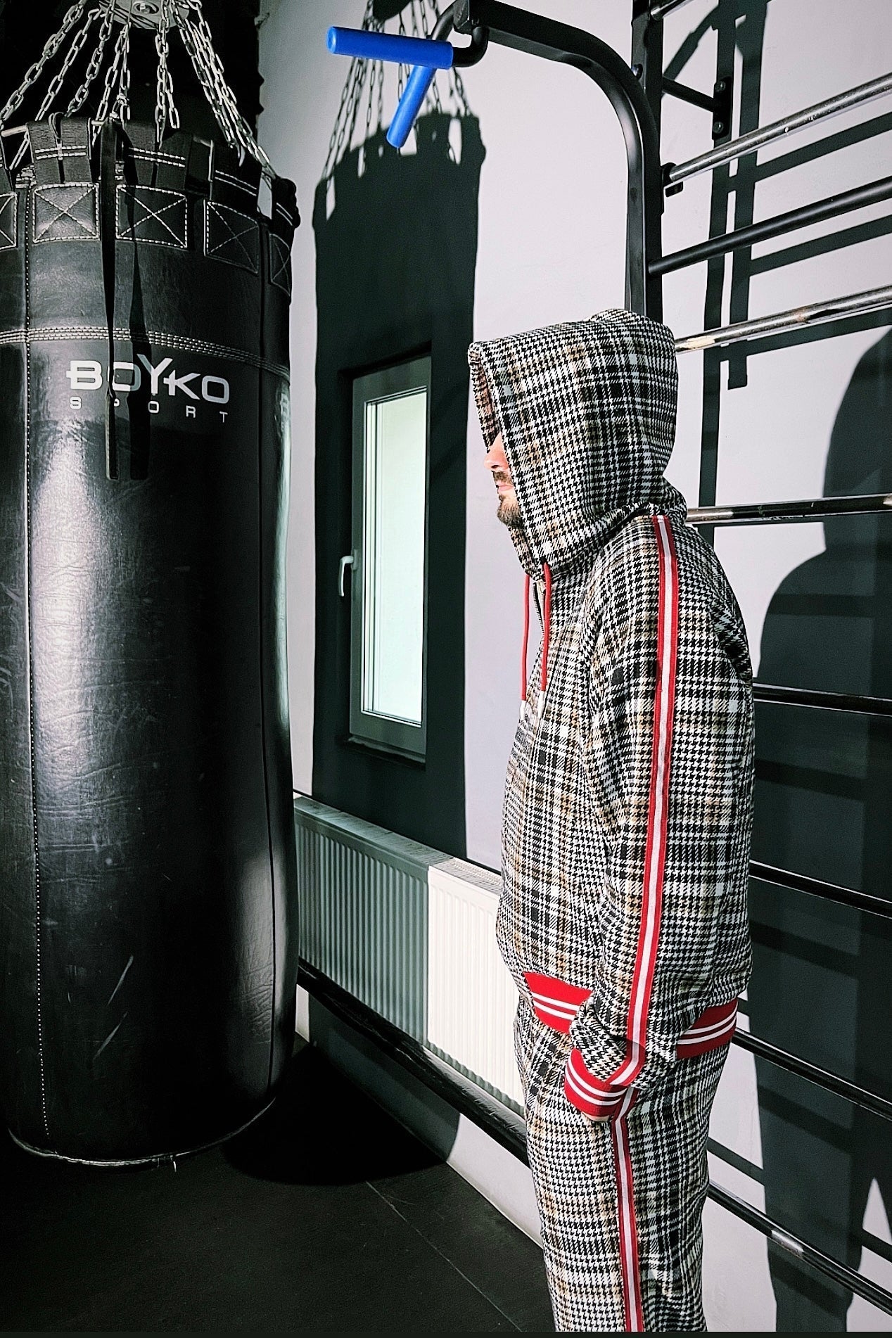 Person in a checkered outfit standing next to a punching bag in a gym.