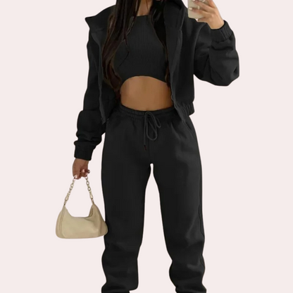 Person wearing a black tracksuit holding a beige handbag on a light pink background
