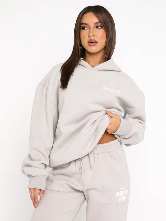 Woman wearing a gray hoodie and pants with branding on a white background