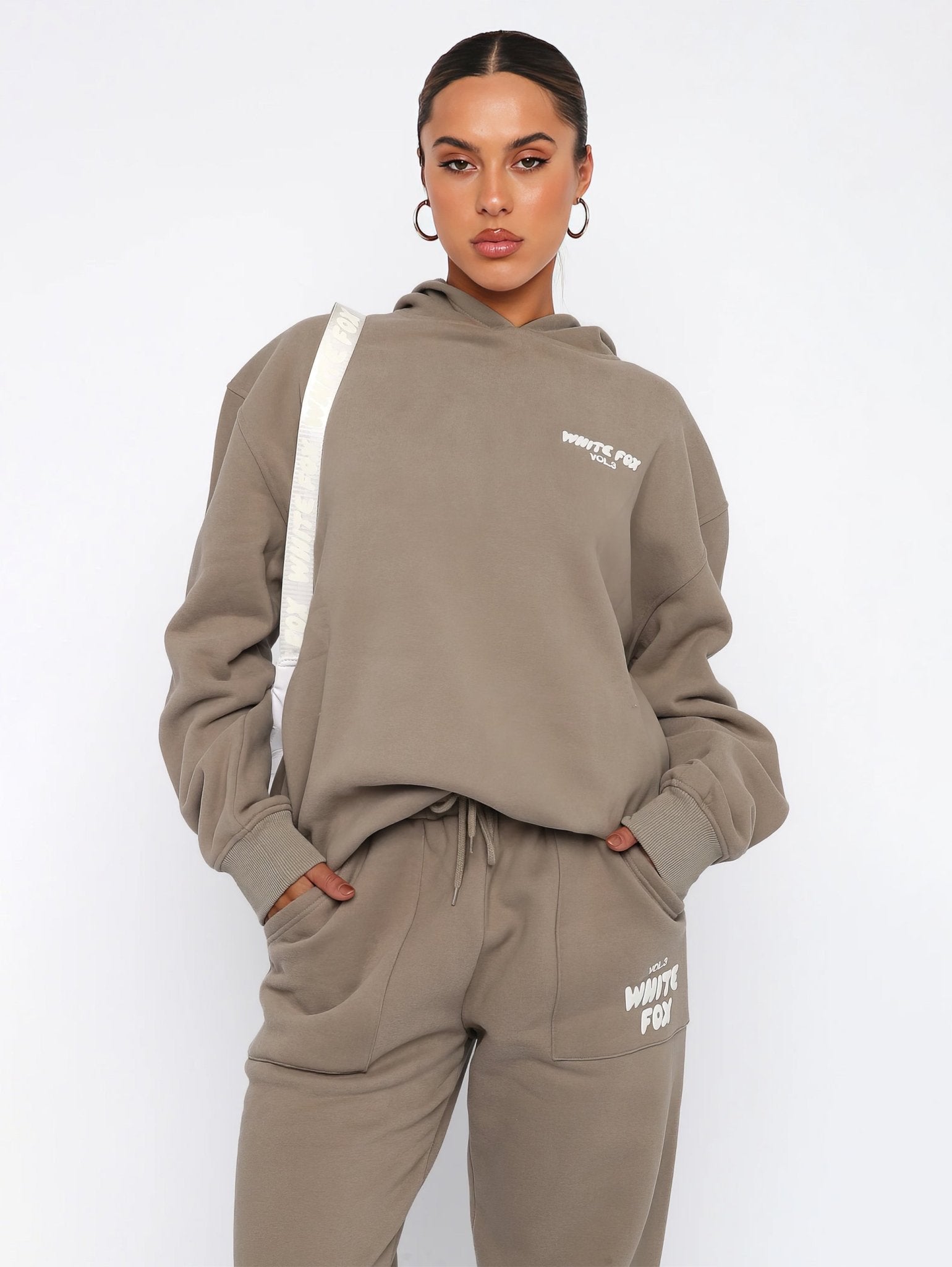 Person wearing a beige hoodie and pants with visible branding on a white background