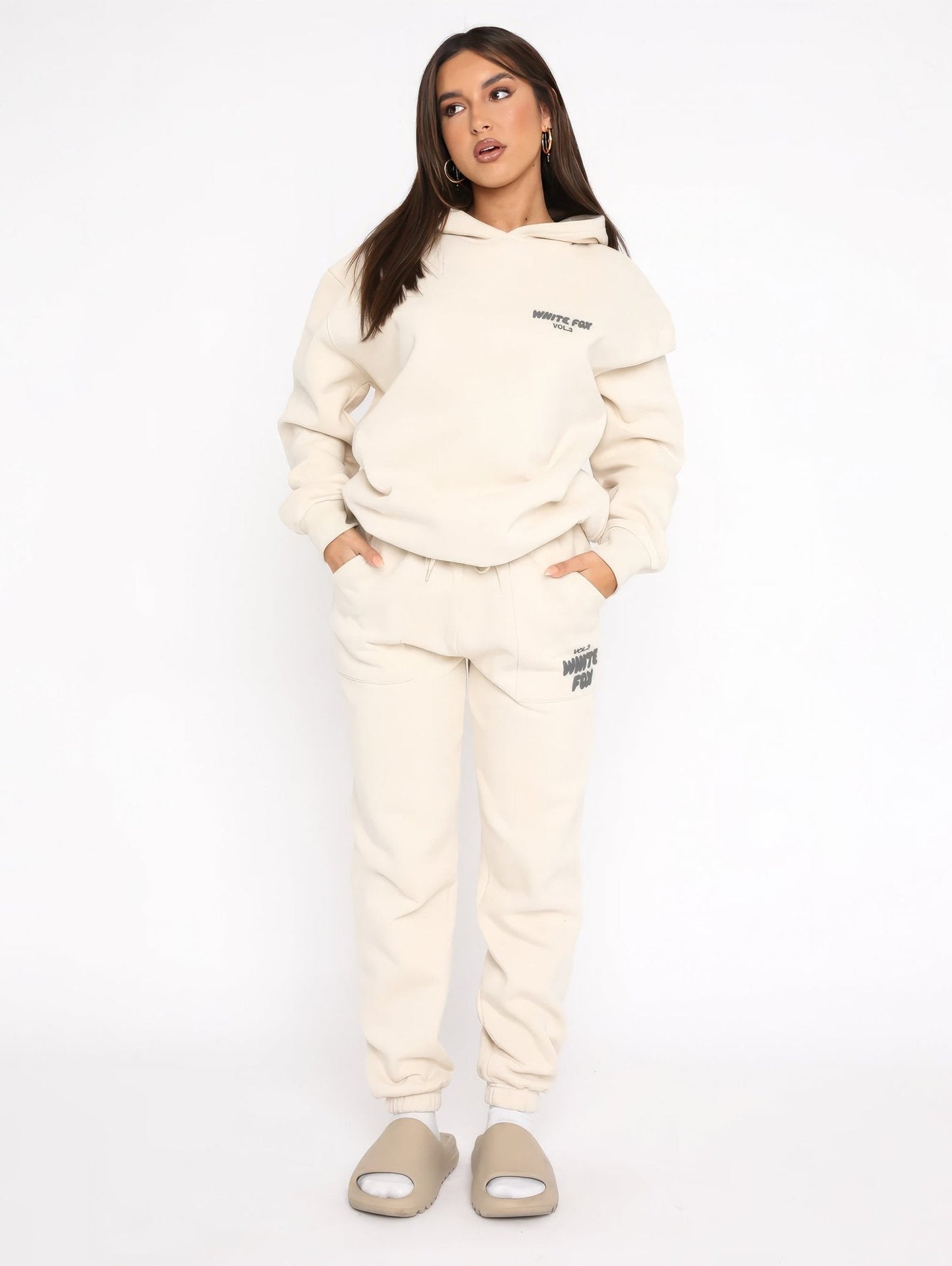 Woman wearing a cream tracksuit with brand logo on a white background