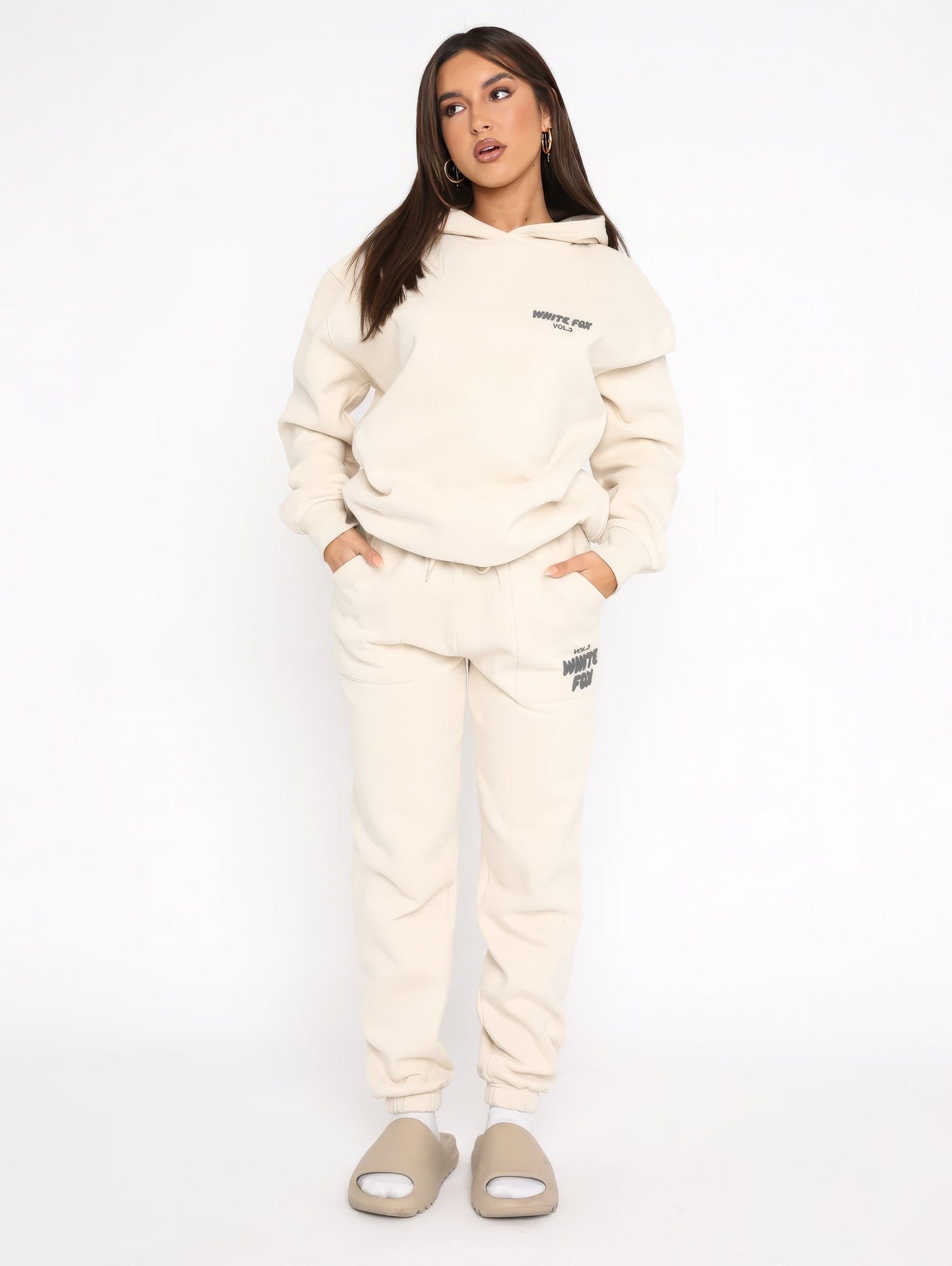 Woman wearing a cream tracksuit with brand logo on a white background