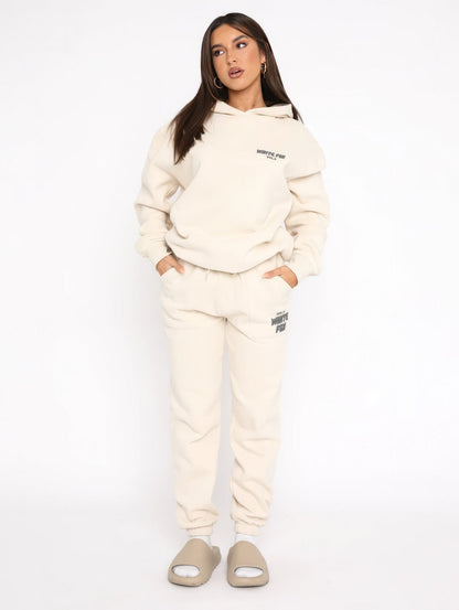 Woman wearing a cream tracksuit with brand logo on a white background