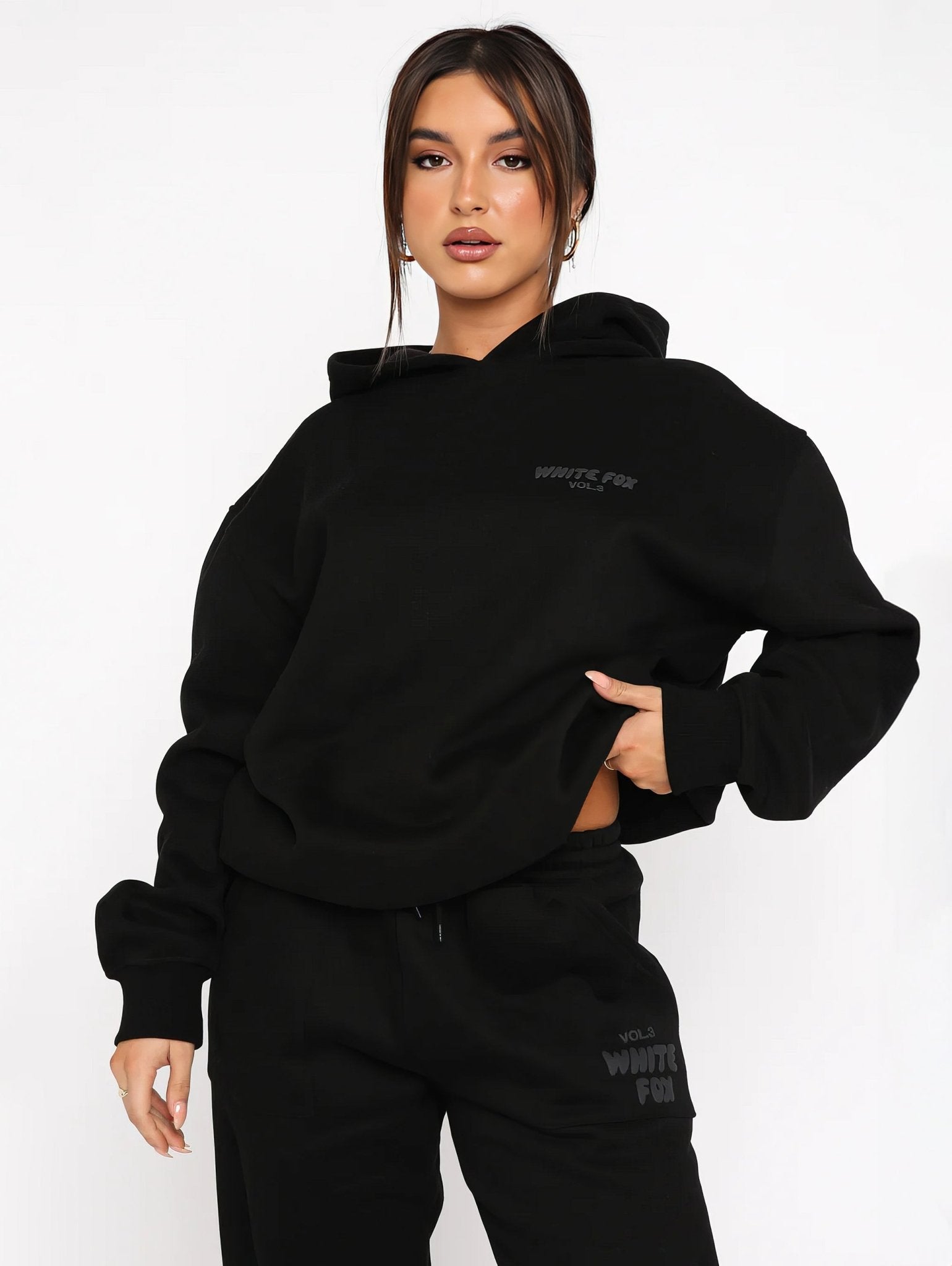 Person wearing a black hoodie and pants with branding on a white background