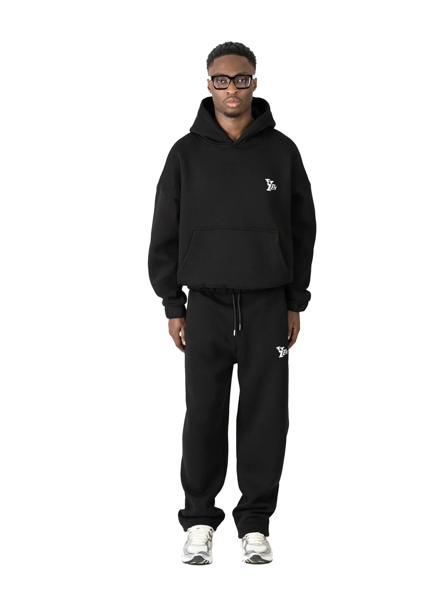 Person wearing a black hoodie and pants with logos on a white background