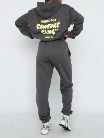 Person wearing a gray hoodie and pants with branding on a white background