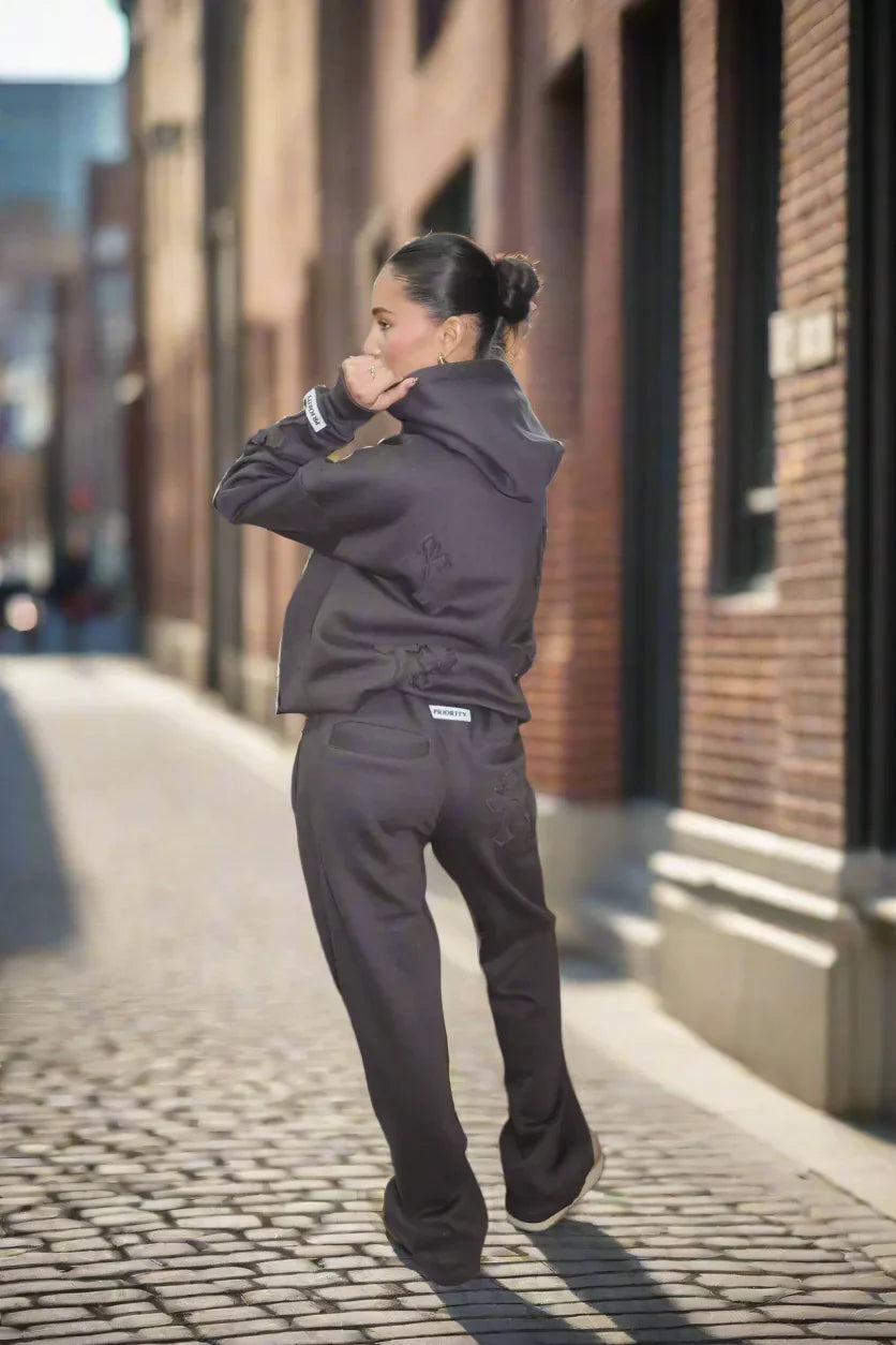 Person wearing a dark gray tracksuit walking on a cobblestone street.